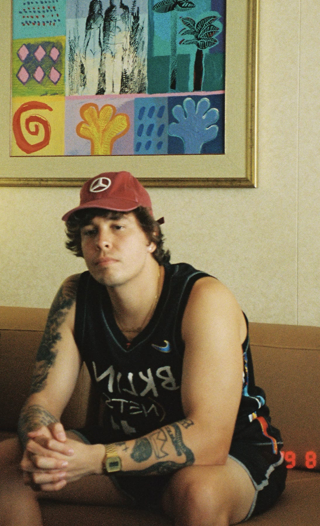 Film photo of Nate Sanway in a red cap sitting under a colorful painting
