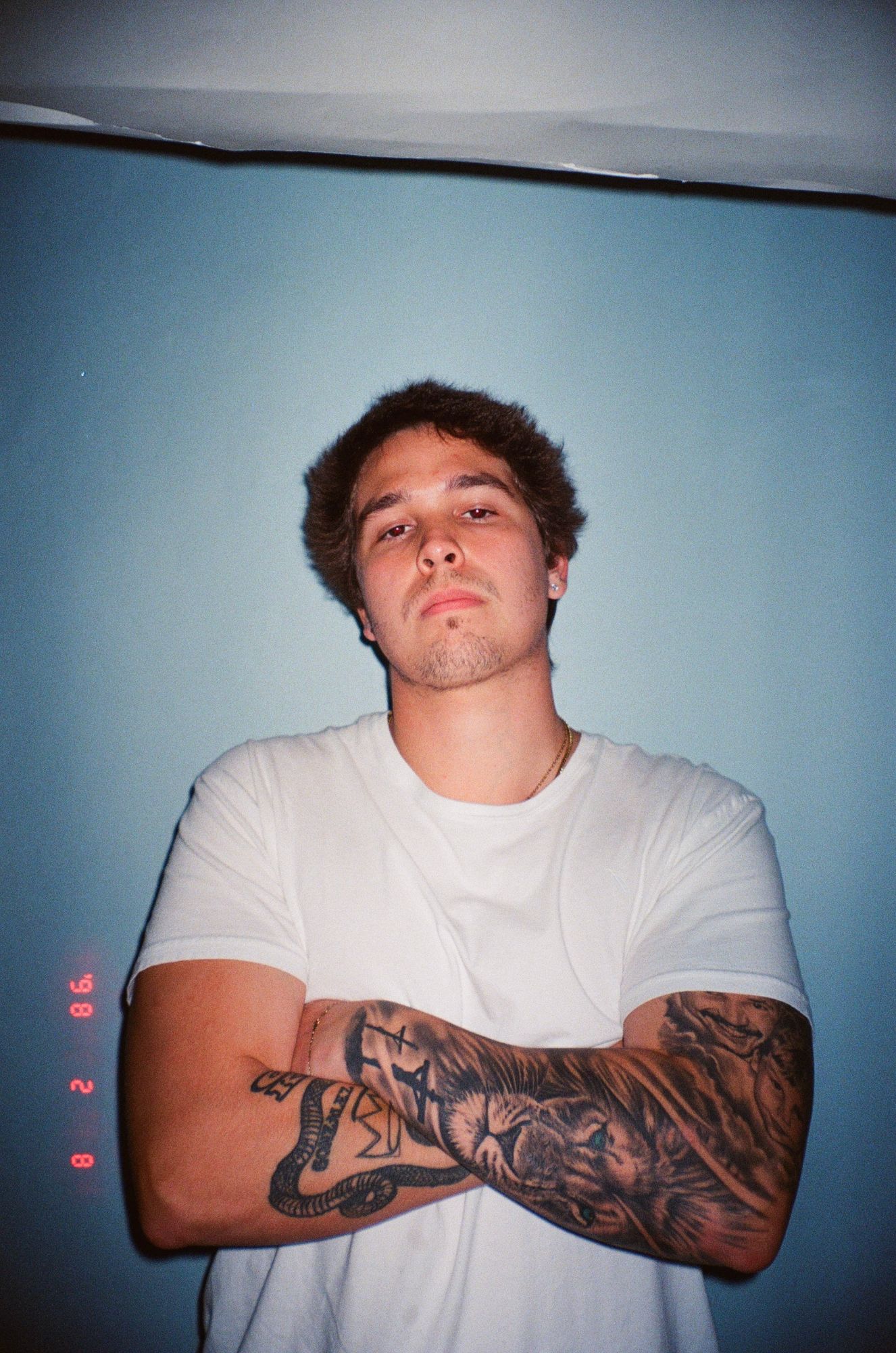 Nate Sanway in a white t-shirt with arms crossed against a blue wall